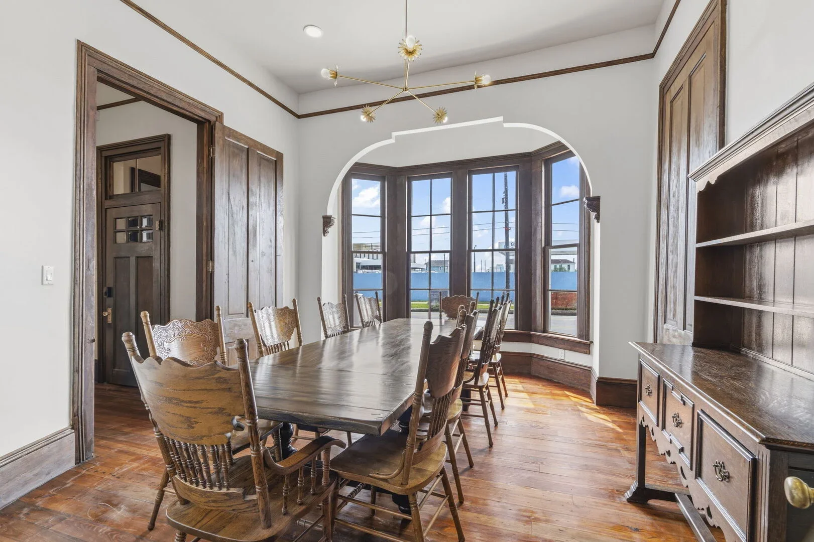 The Mollie Walters Dining Hall a large wooden table surrounded by wooden chairs, a wooden China cabinet, and a large bay windows letting in natural light.