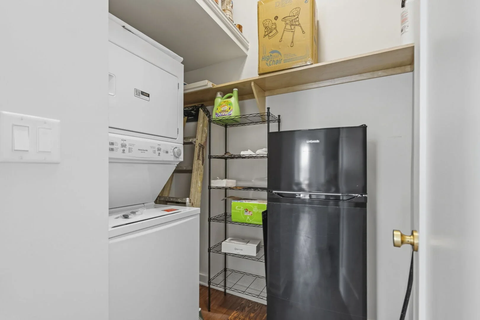 Mollie Walters House laundry room with a stacked washer and dryer, a black metal shelving unit, and black mini fridge