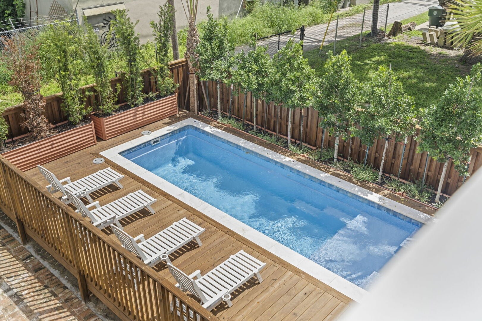 An aerial view of the Mollie Walters House backyard swimming pool with a wooden deck and white lounge chairs.