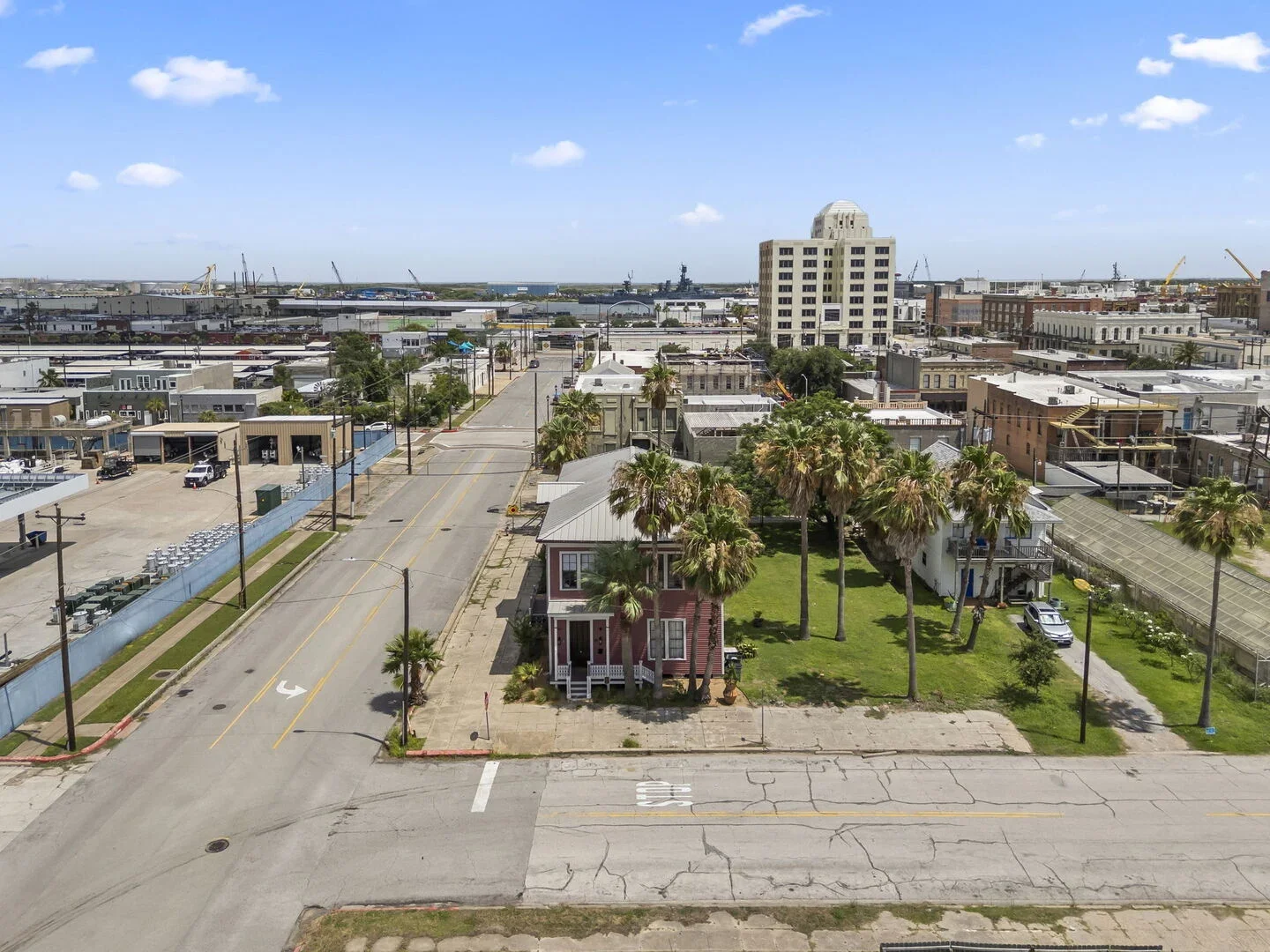 Aerial view of a city with restored 1886 Mollie Walters House with a distant harbor and cranes under a partly cloudy sky.