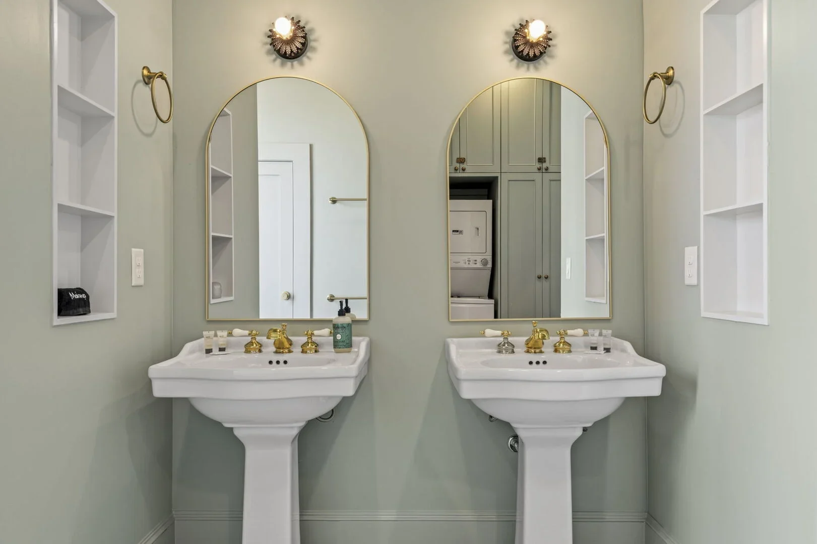 Mollie Walters House upstairs bathroom featuring celadon-colored tiles, a toilet, two pedestal sinks, a shower, a stacked washer and dryer, and a wall-mounted cabinet