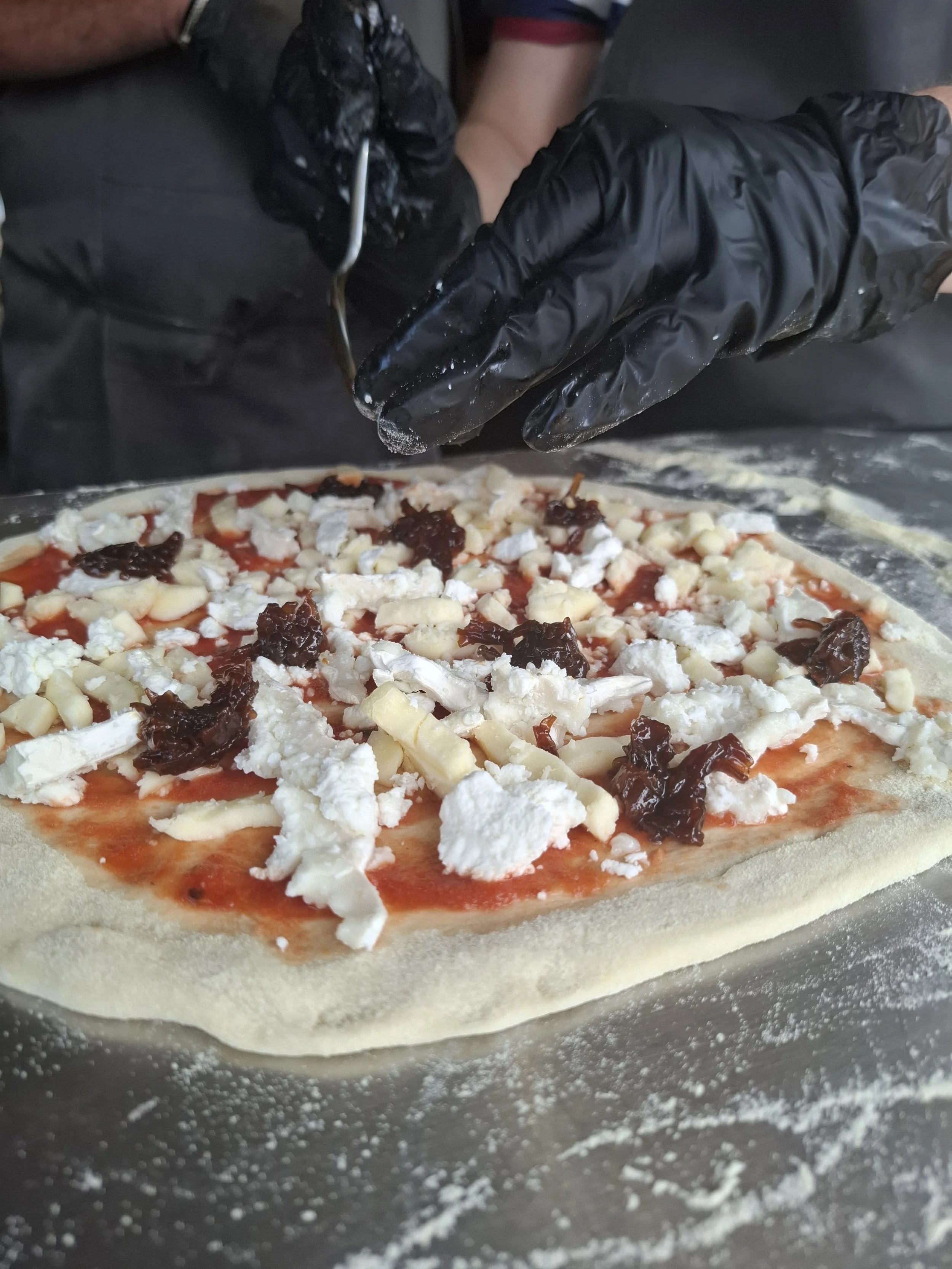 A pizza dough on a baking surface with various toppings including cheese, tomato sauce, and dark toppings, being prepared for baking.
