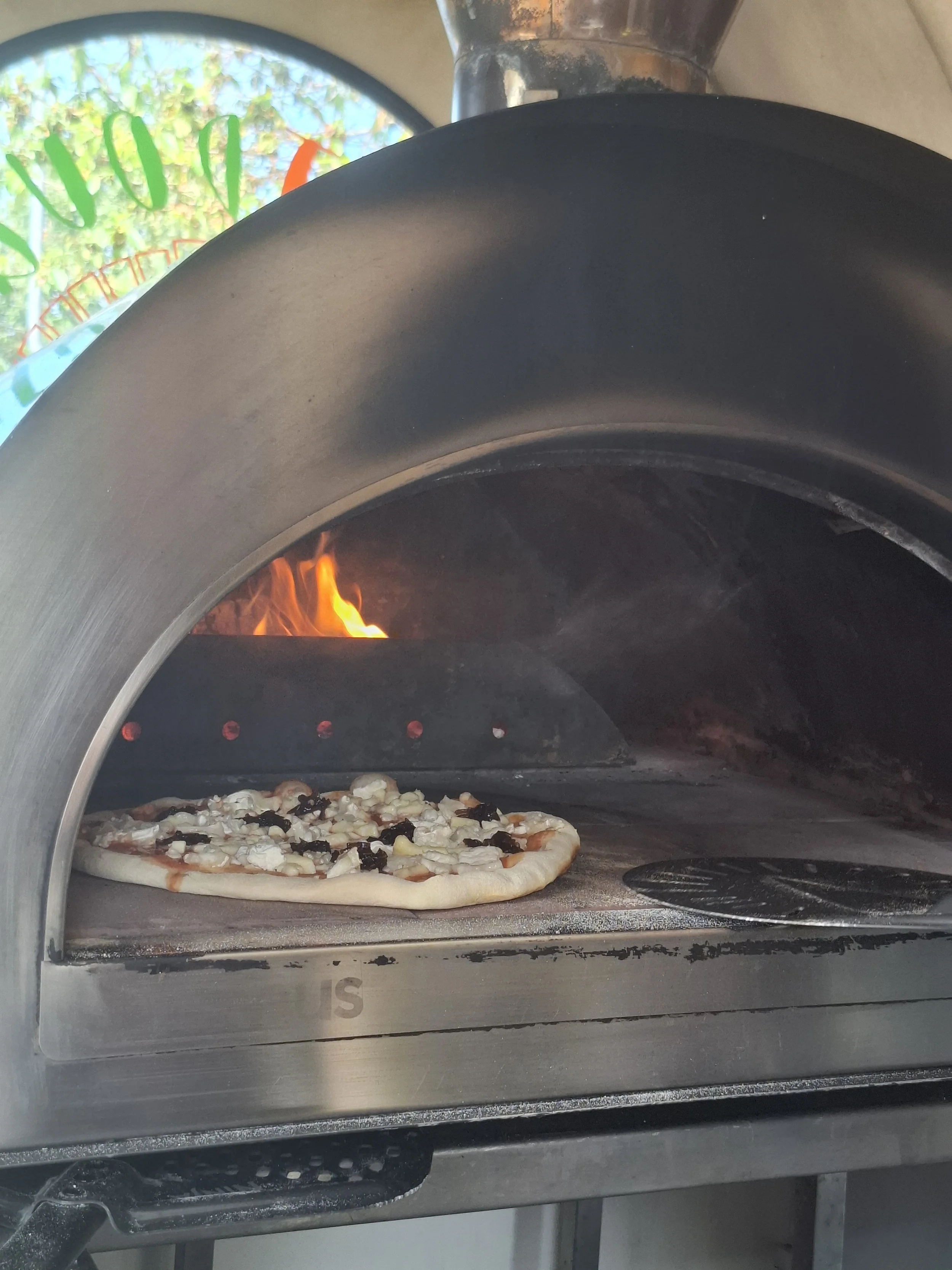 A pizza baking inside a commercial pizza oven with an open door, showing cheese and toppings on the pizza.