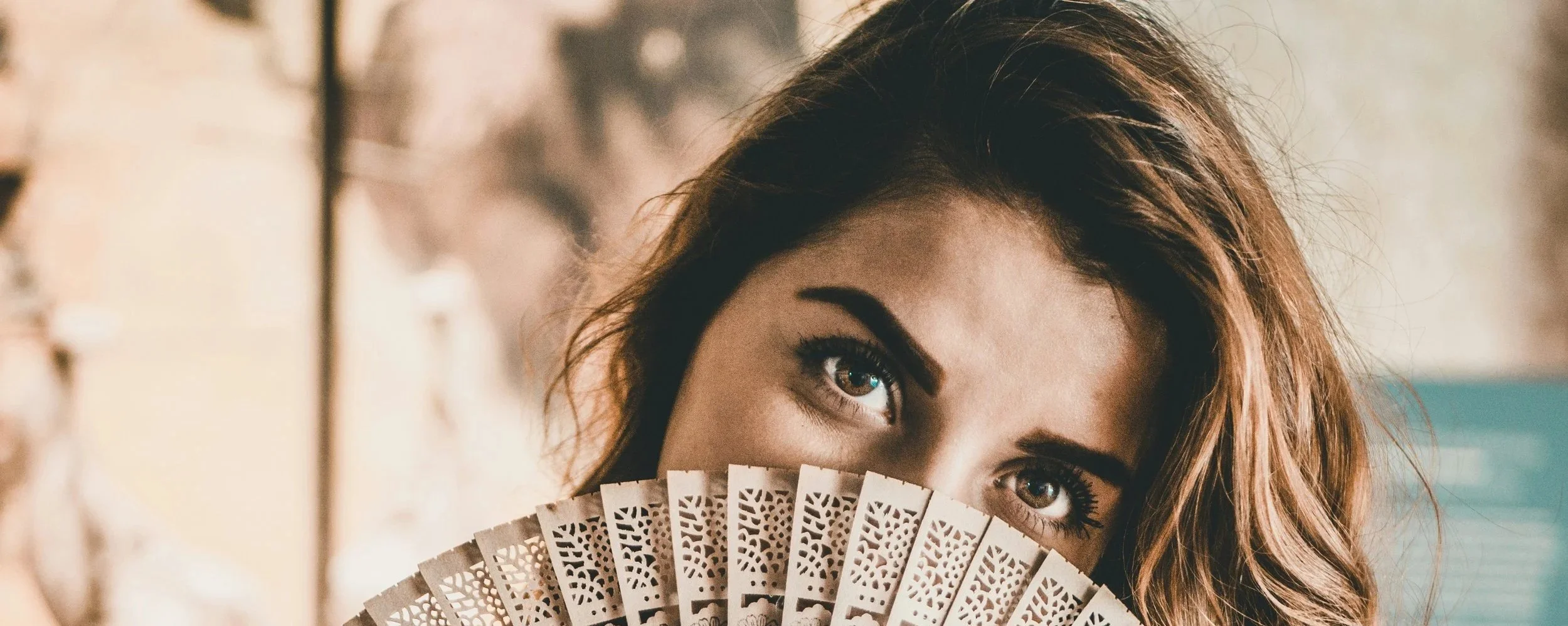Woman smiling behind a decorative fan with defined eyebrows