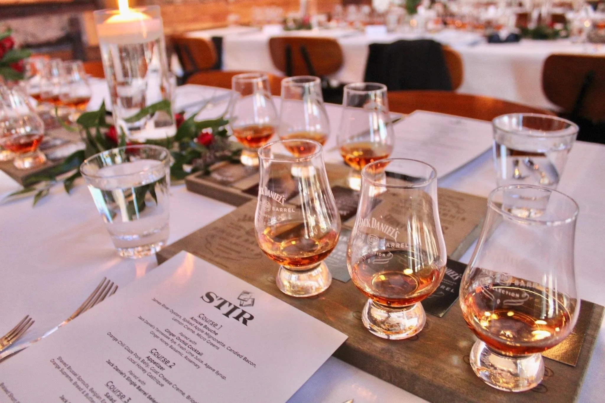 A table set for a whiskey tasting event with several glasses of whiskey, a candle, and a menu on the table.
