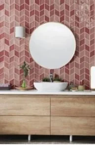 Salle de bains avec un miroir rond, lavabo, étagère avec plantes et accessoires, murs en carreaux hexagonaux roses
