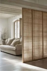 Espace intérieur avec un canapé beige près d'une fenêtre et une paroi en bois tressé qui sert de séparation
