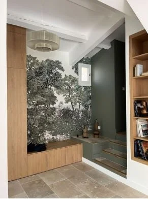 Mur avec une grande fresque d'arbres, étagère en bois, escaliers, et meuble de rangement en bois dans un intérieur moderne.