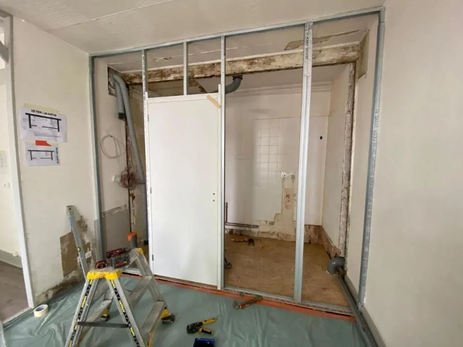 Travaux de rénovation d'une pièce avec une cloison en cours de construction, outils, escabeau, et matériaux de construction présents. Travaux et conception suivi par par Nadine Agencement & Design, architecte d'intérieure et décoratrice à Mions