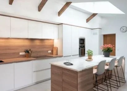 Cuisine moderne avec un îlot central en bois, chaises blanches, armoires blanches, lampe de plafond et une plante avec des fleurs.