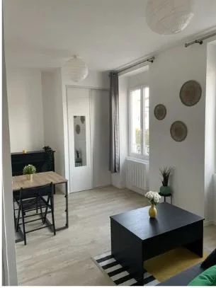 Salon lumineux avec table, chaises, canapé, murs décorés avec plateaux, et une grande fenêtre