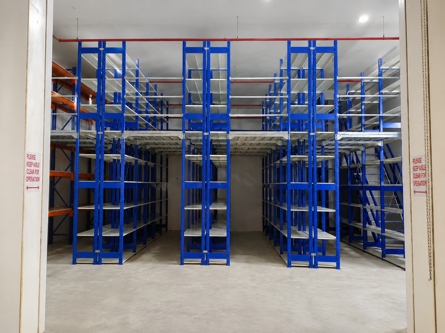 Empty storage room with blue and orange metal shelving units, warning signs on doorframe
