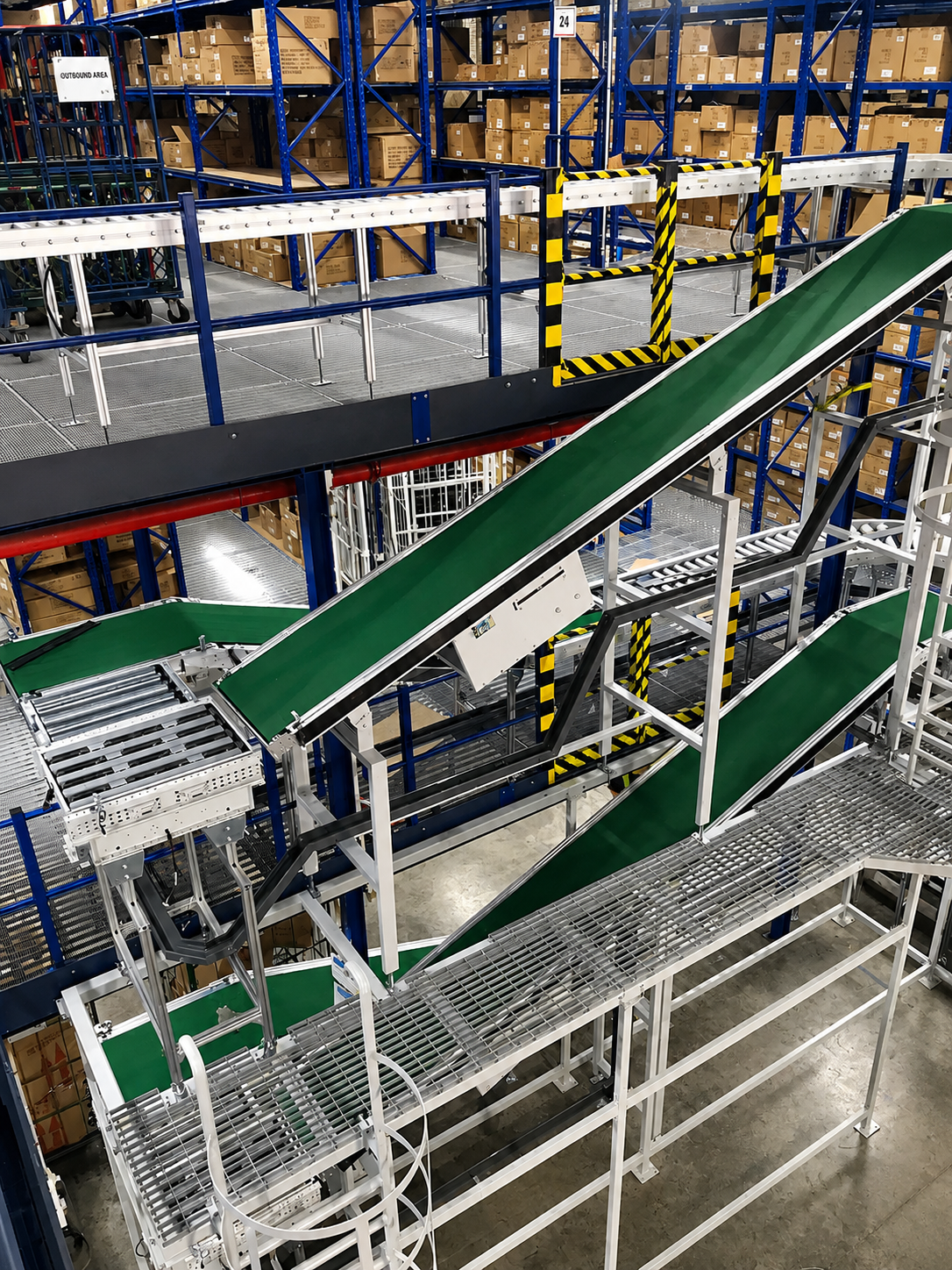 View of a warehouse with metal shelves filled with cardboard boxes, a green conveyor belt, and a staircase.