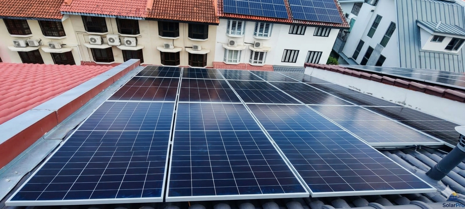 Multiple solar panels installed on the rooftop of a residential building with other rooftops and buildings visible in the background.