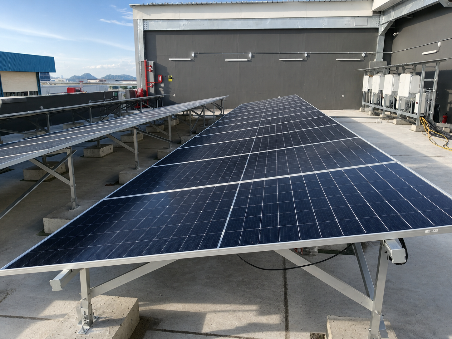 On the rooftop of a building, there are multiple solar panels installed, including one large solar panel in the foreground and smaller ones to the side, with a cityscape in the background and clear skies.