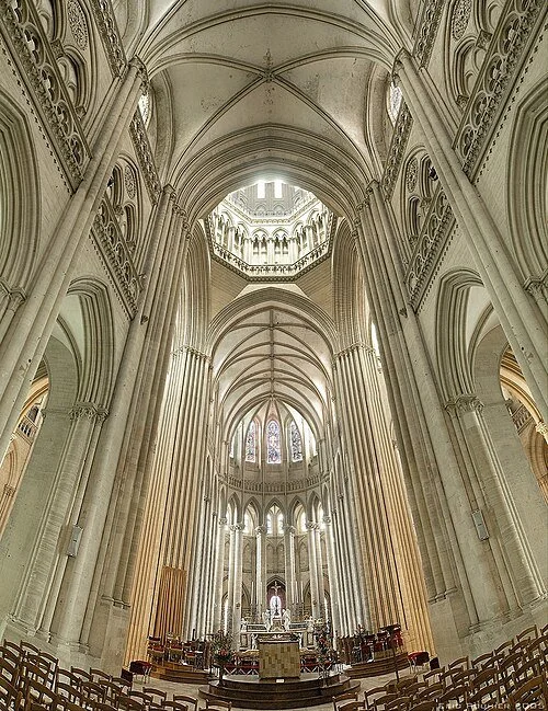 Interior of a grand Gothic cathedral with tall, pointed arches, high vaulted ceilings, and intricate stone detailing, illuminated by natural light through stained glass windows.