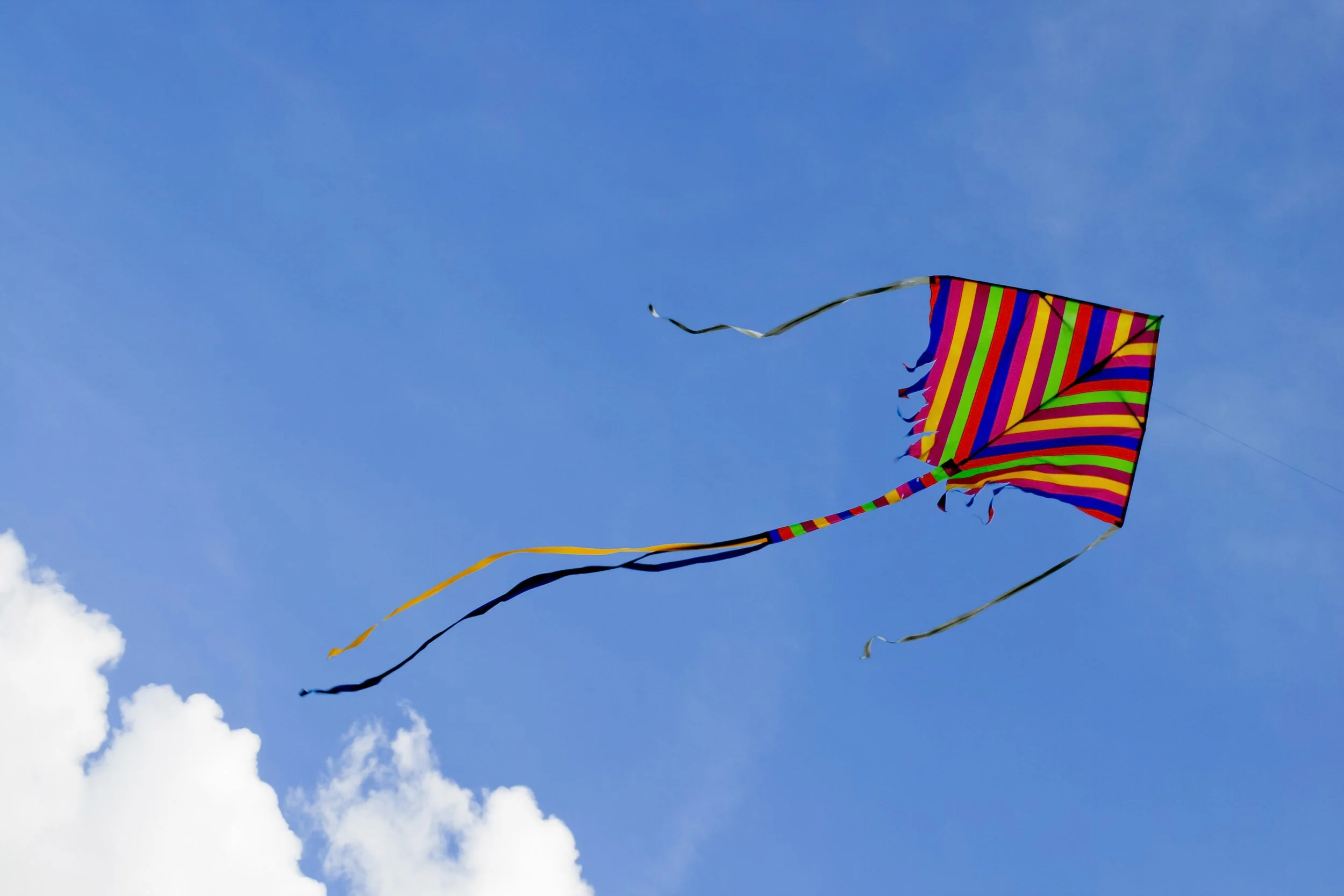 Colorful striped kite flying in a clear blue sky with some white clouds.