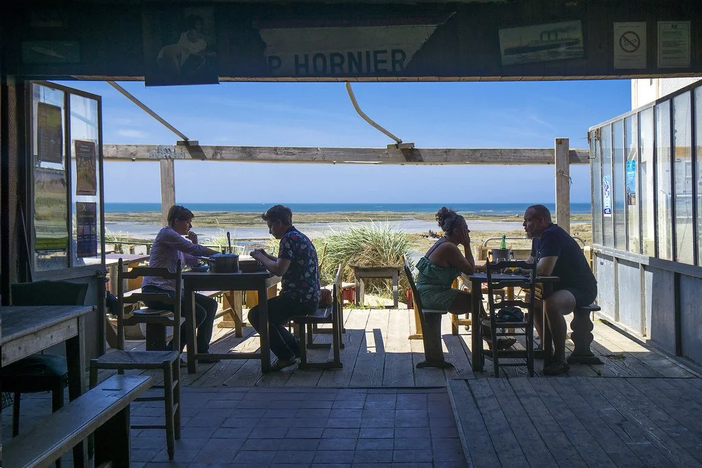 People dining at a seaside restaurant with a view of the beach and ocean in the background.