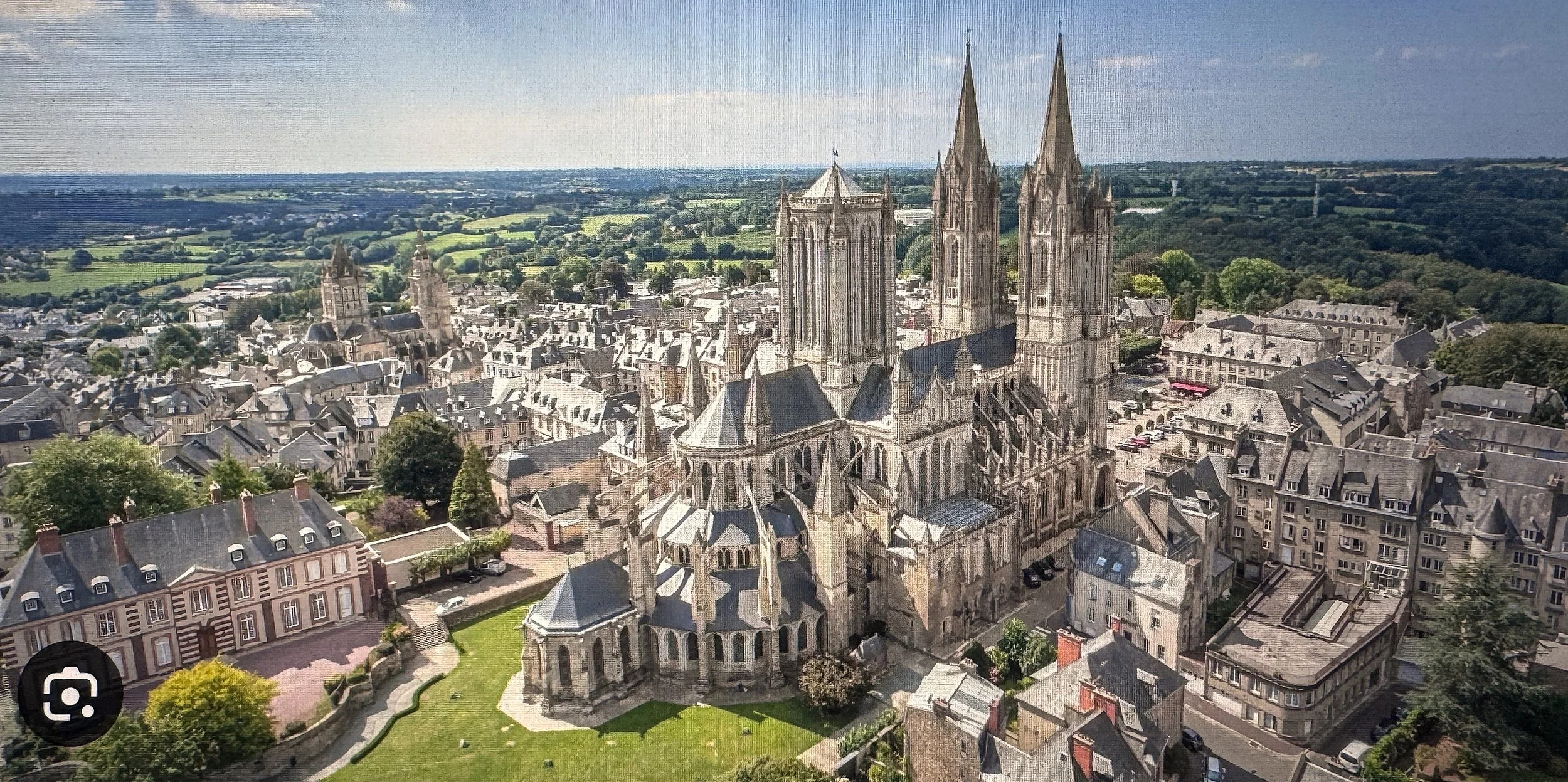 Aerial view of a historic cathedral with tall spires, surrounded by traditional European buildings and green landscape.