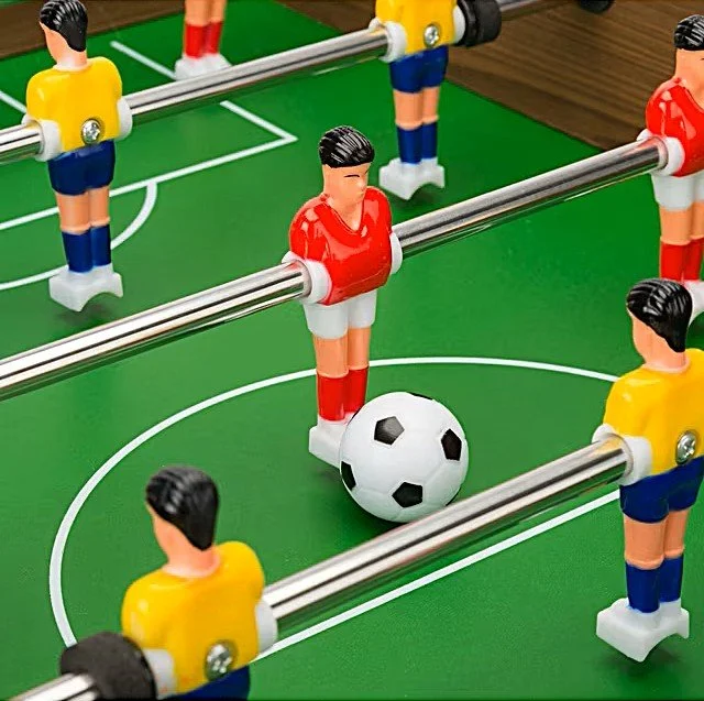 Foosball table with plastic soccer players, a black-and-white soccer ball, and a green playing surface.
