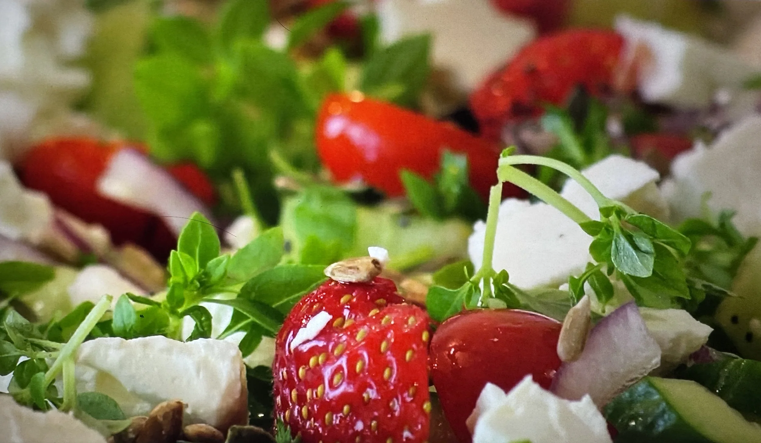 Close-up of fresh strawberries, green herbs, sunflower seeds, and white flower petals on a surface.