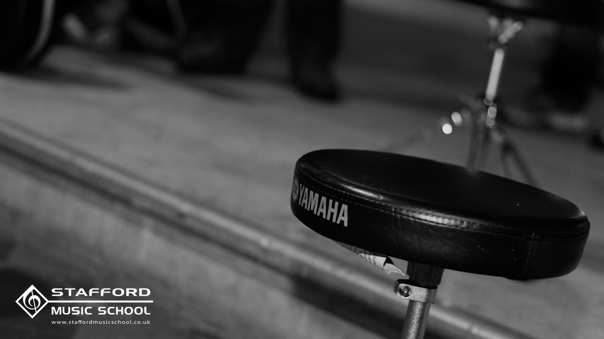 Black Yamaha stool in a music studio with Stafford Music School logo and website