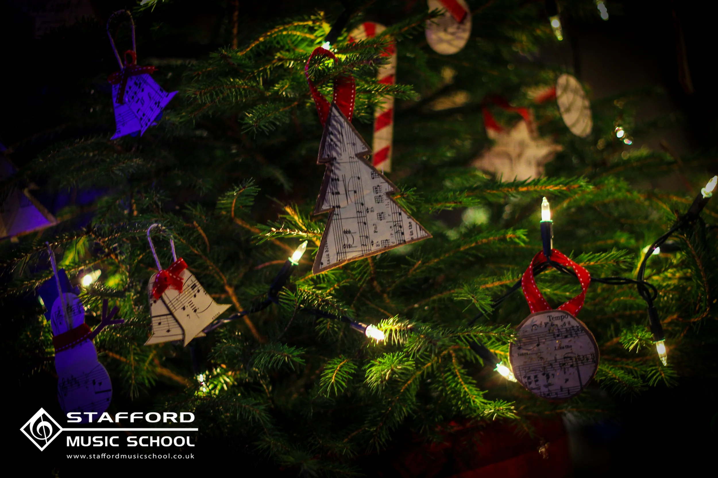 Christmas tree decorated with music note ornaments, candy cane ornaments, and colorful lights. The bottom left corner features a logo for Stafford Music School and their website.
