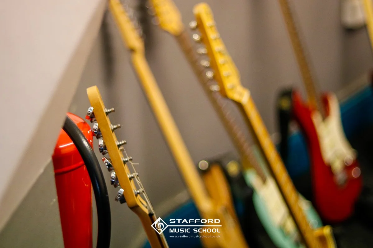 Guitars hanging on a wall with a red fire extinguisher nearby at Stafford Music School.