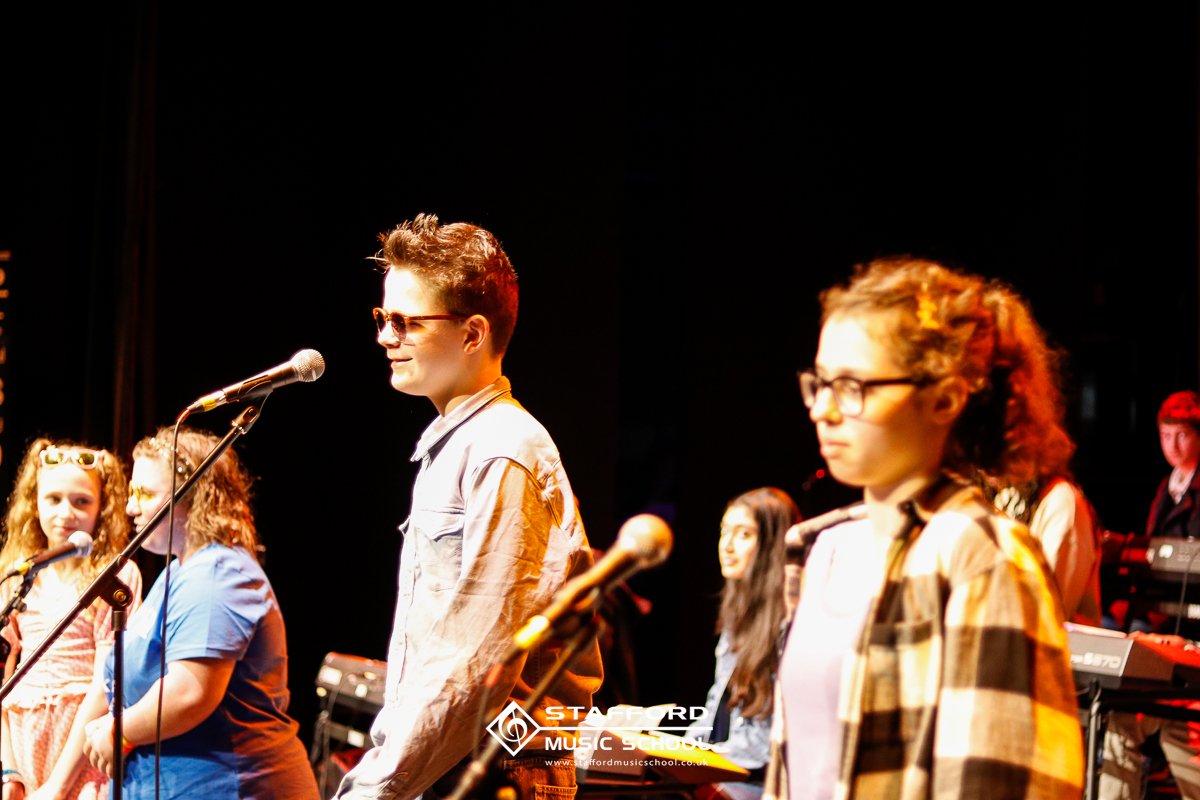 Young students standing on stage with microphones during a performance.
