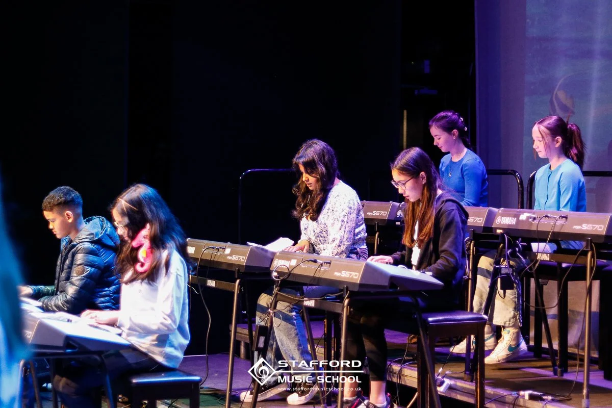 Group of young students playing electronic keyboards on stage at Stafford Music School.