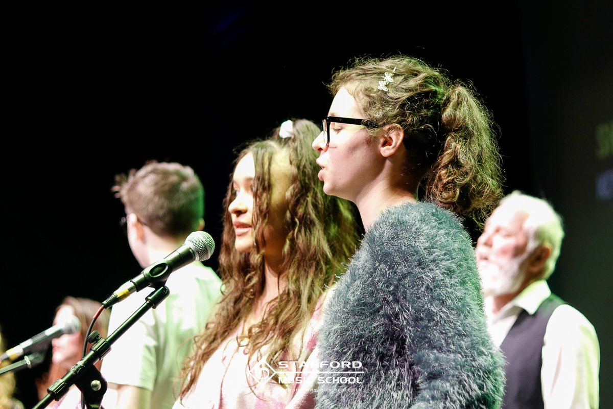Group of diverse people standing in a row with microphones, listening, during a music or school event.