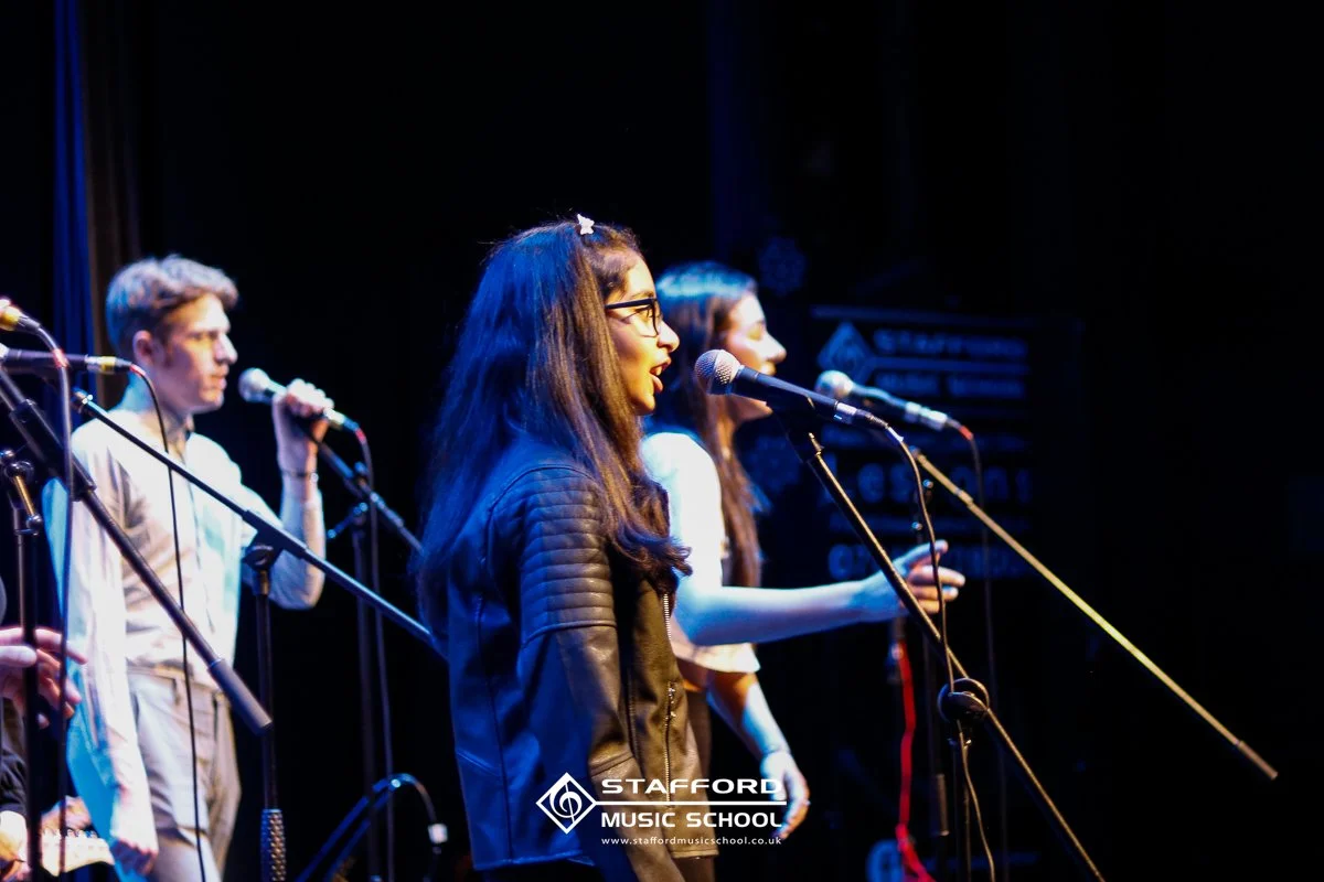 Group of young people singing into microphones on stage at Stafford Music School