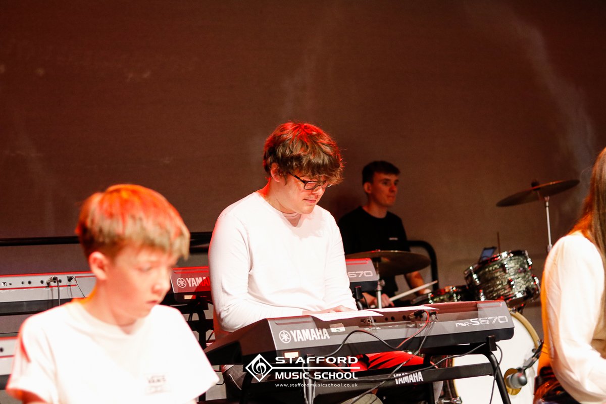 Young male musician with glasses playing a Yamaha keyboard on stage during a music school performance