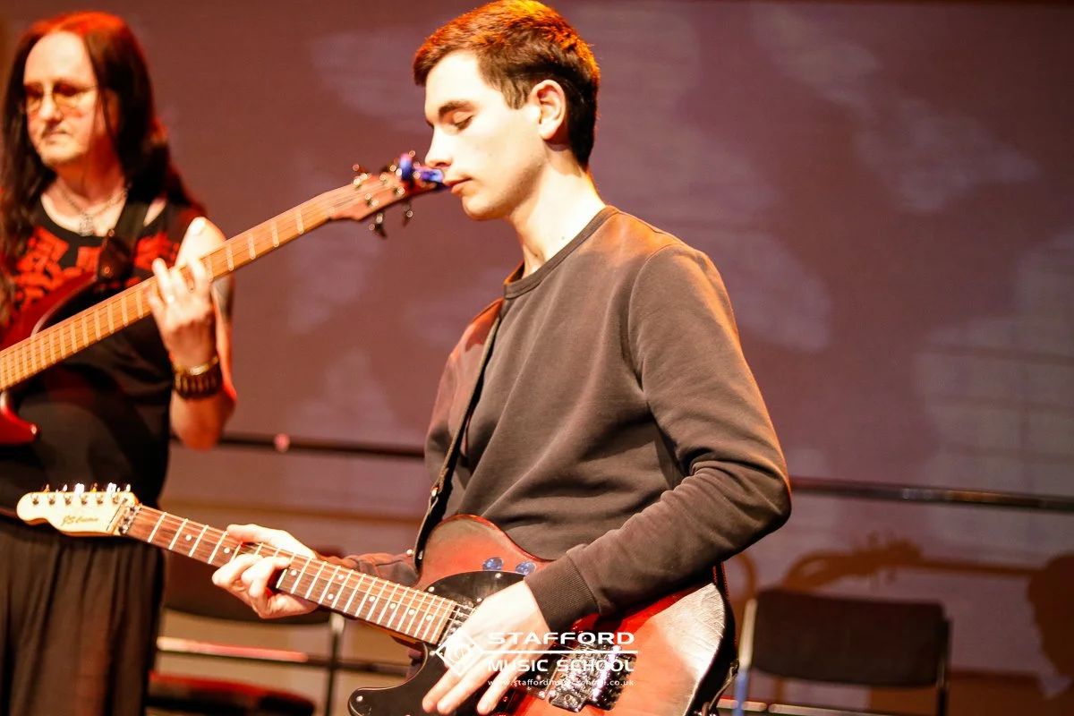 Two young men playing electric guitars on stage during a music performance