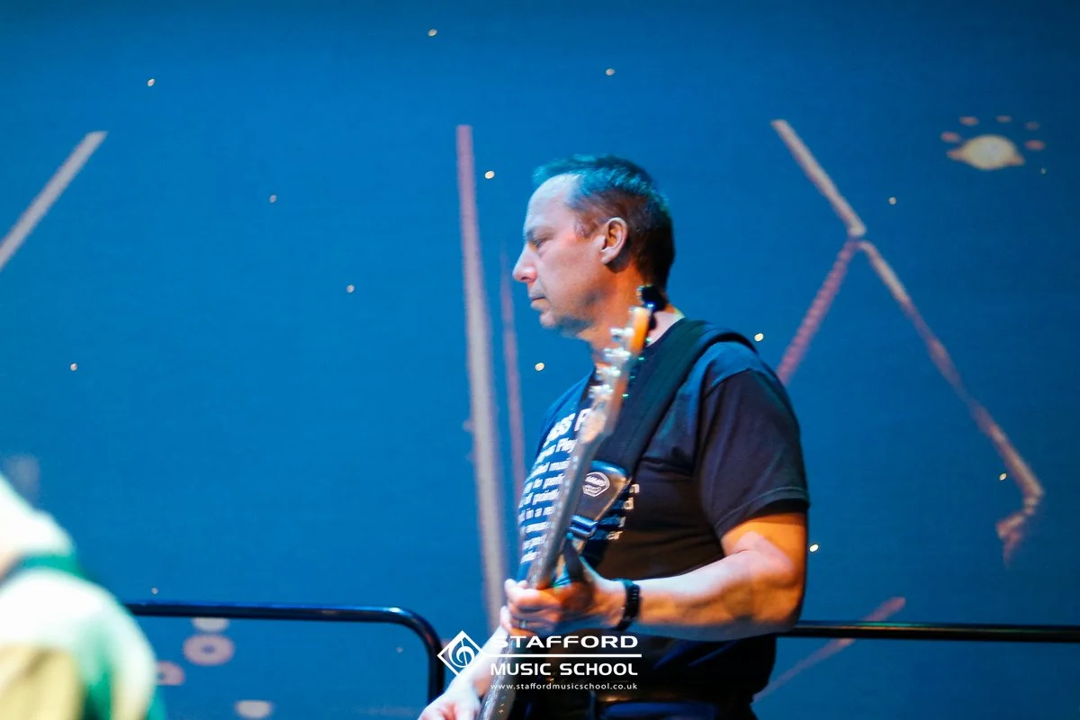 A man playing an electric guitar on stage, with a starry night sky background projected behind him.