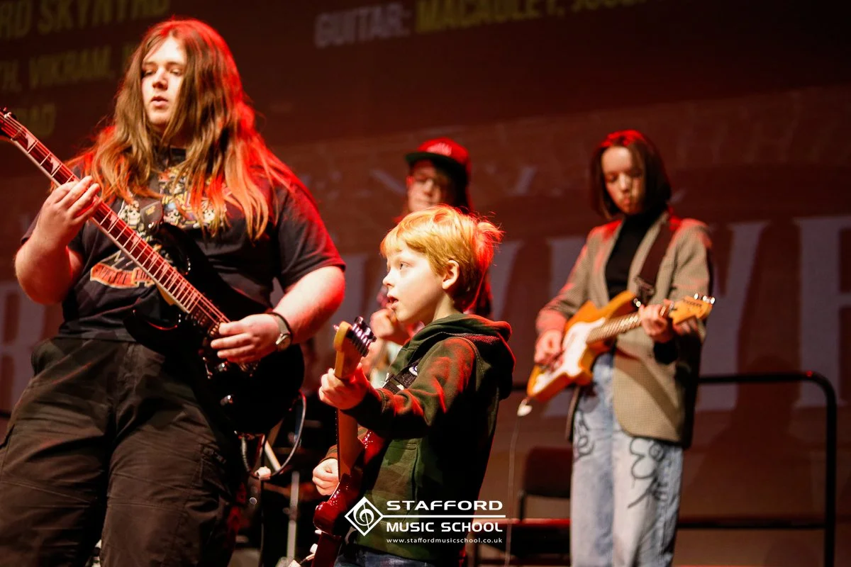 Young students playing electric guitars on stage at Stafford Music School.