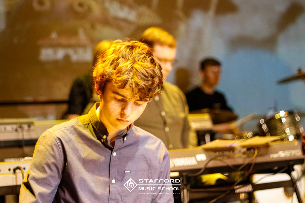 Students playing keyboard instruments at Stafford Music School, with a young man in the foreground and others in the background.