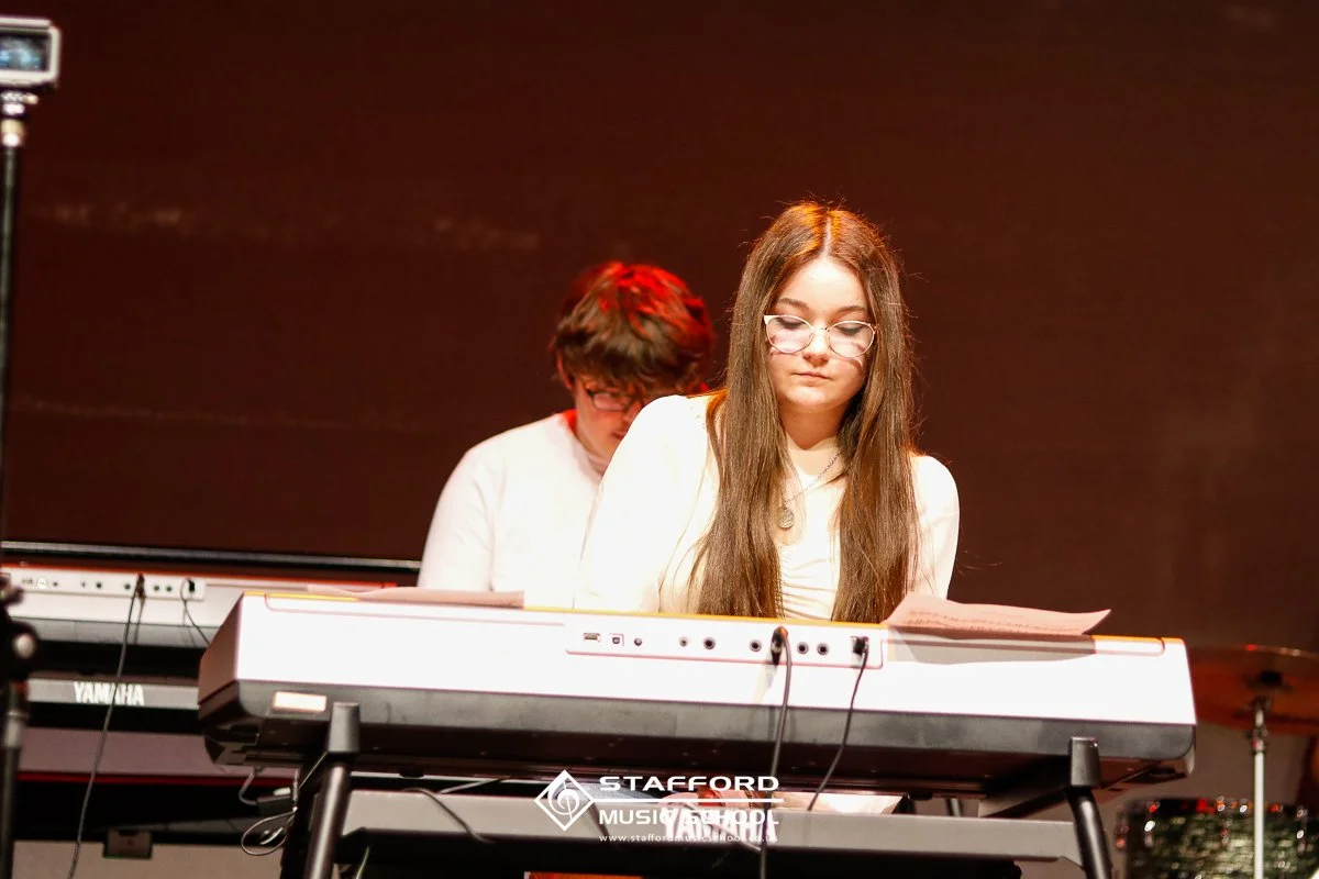 Two young women playing keyboard on stage during a performance at Stafford Music Festival.