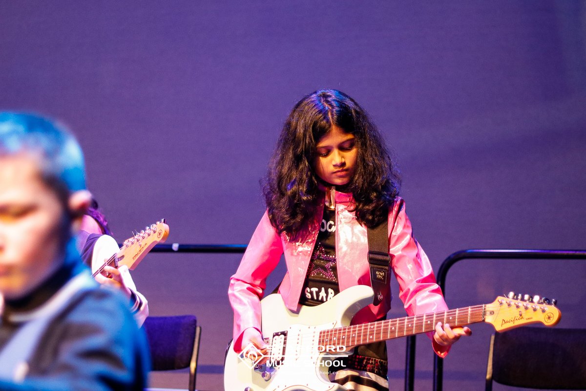A young girl playing an electric guitar on stage during a performance.