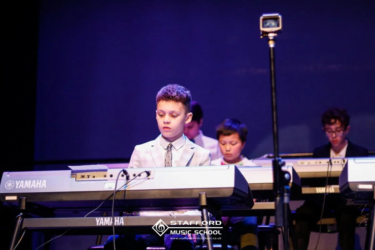 Young boys performing on stage with Yamaha keyboards during Stafford Music School event.