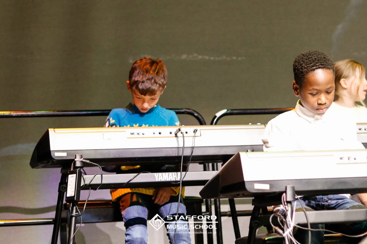 Children playing Yamaha electric pianos on stage at Stafford Music School.