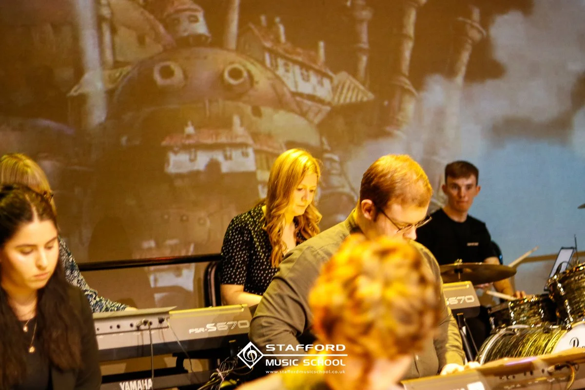 Music students practicing at Stafford Music School, with a backdrop of a Studio Ghibli film scene projected behind them.