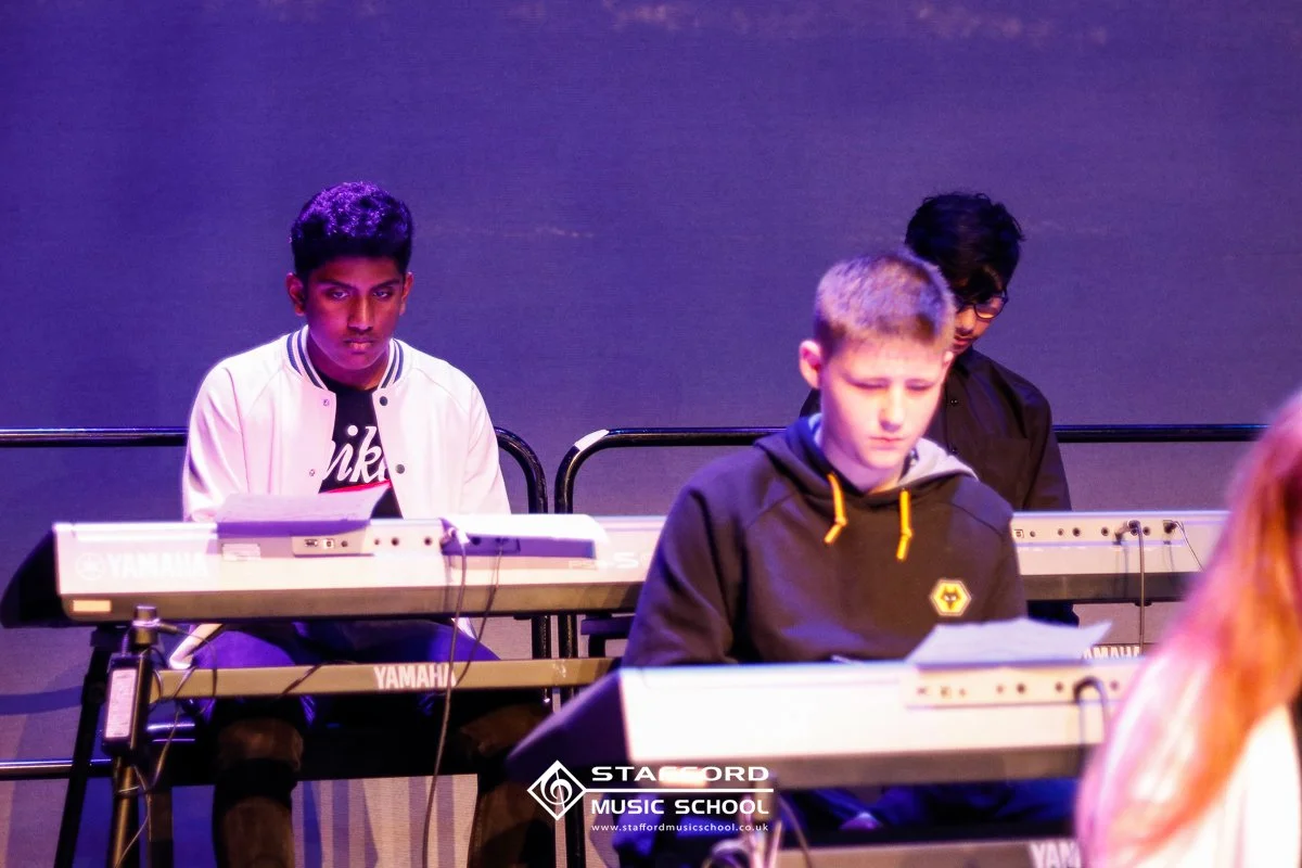 Three young males playing Yamaha keyboards during a music class at Stafford Music School.