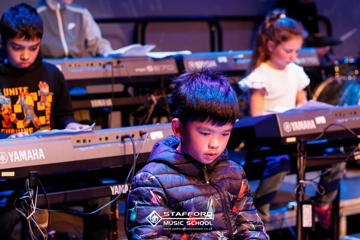 Young children practicing on Yamaha keyboards during a music class at Stafford Music School.