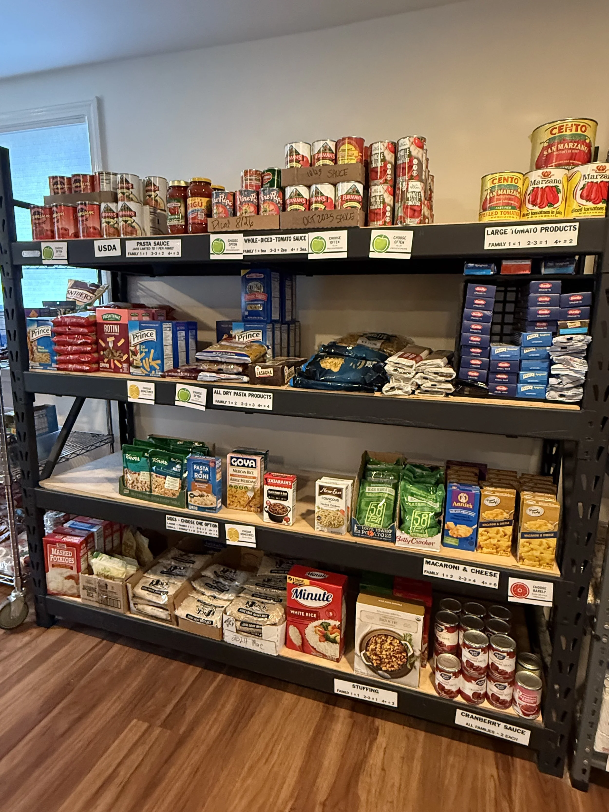 Shelf with various canned and boxed food products including tomato sauce, dried pasta, rice, stuffing, and cranberry sauce, labeled with categories for easy selection.