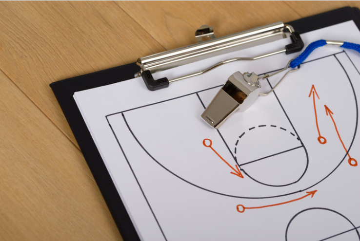Basketball coach's shot chart on clipboard with a clipboard clip and a whistle on a wooden floor.