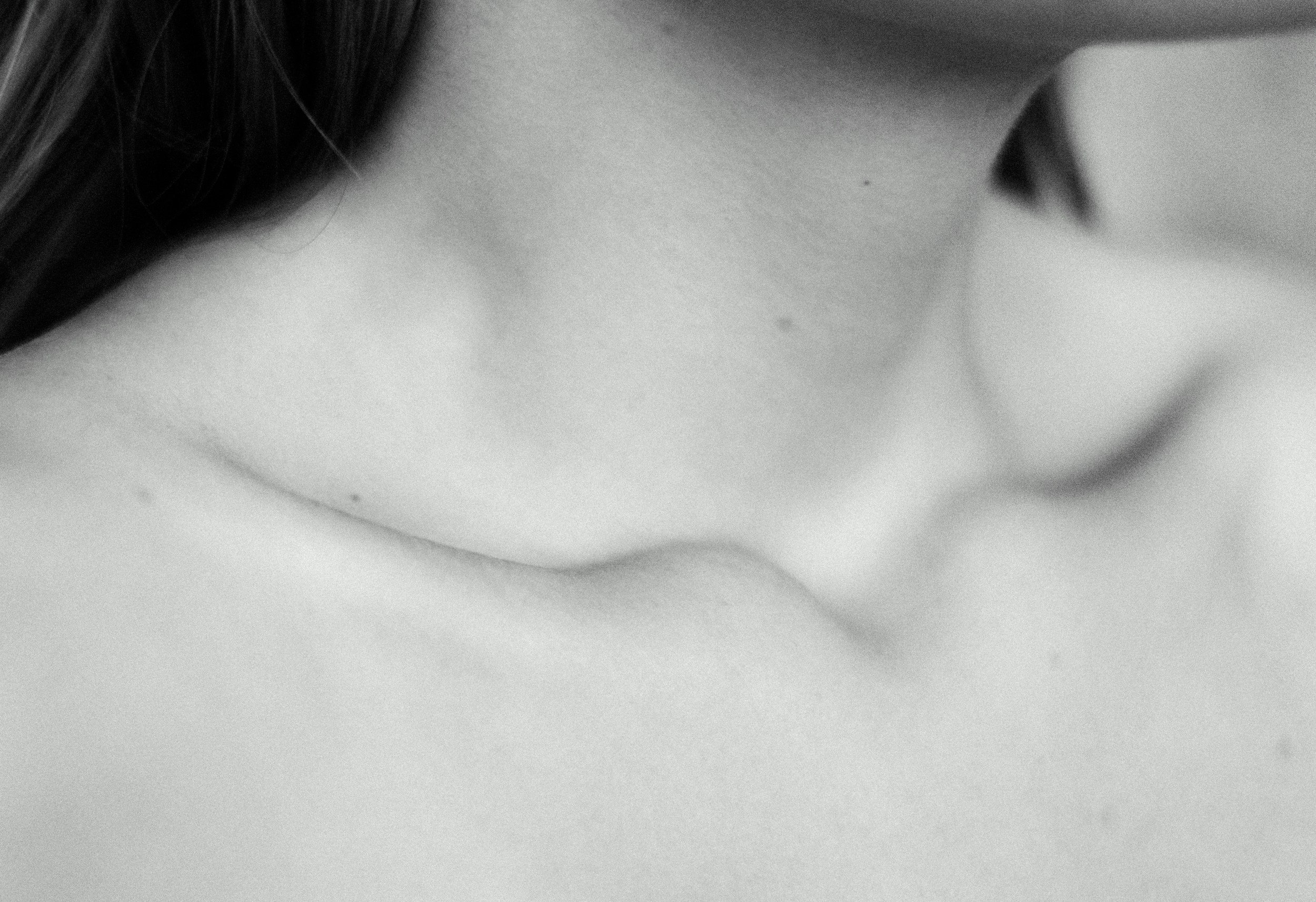 Close-up of a person's neck and cheek, with dark hair partially visible on the left side of the image, in black and white.