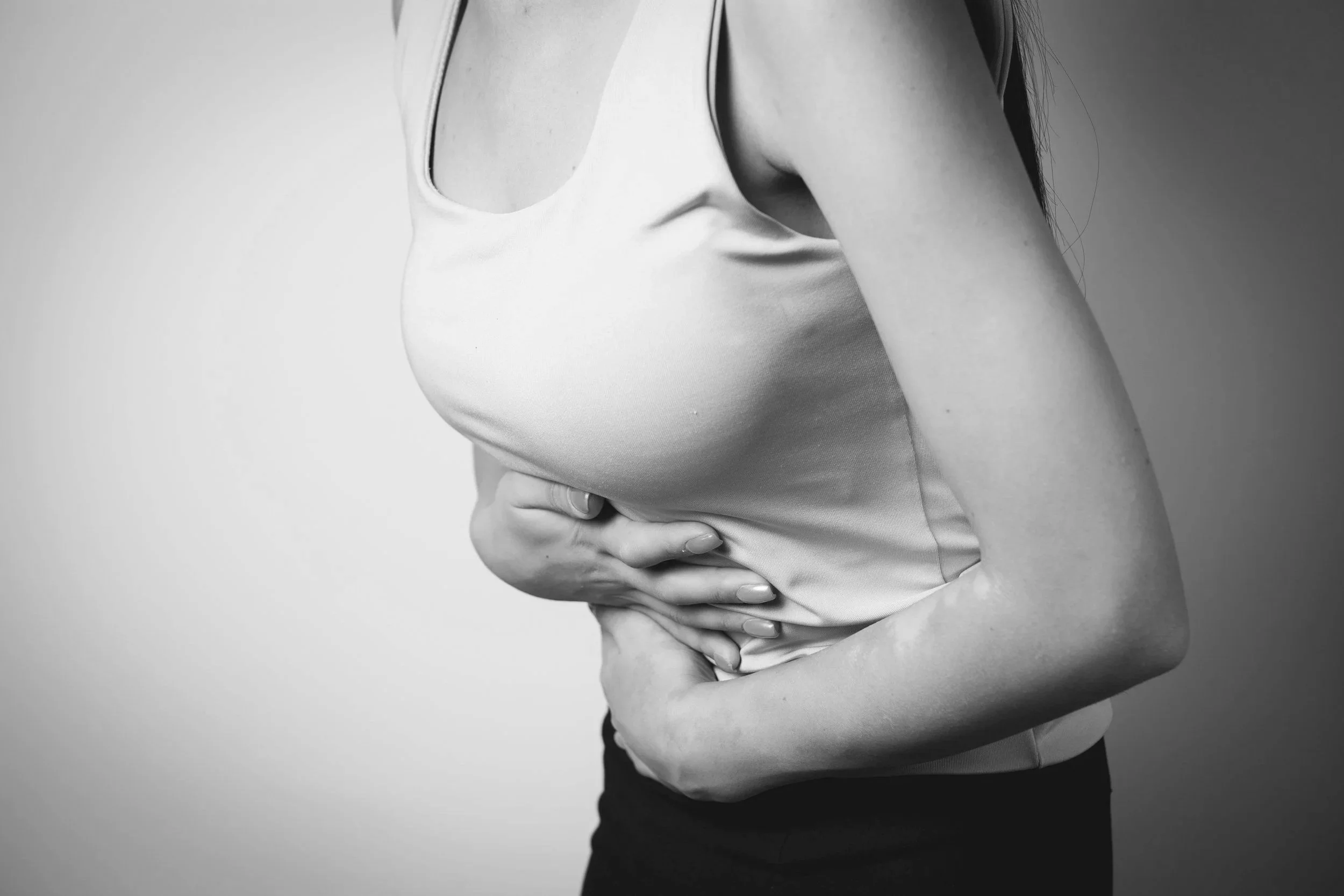 A person in a sleeveless top clutching their stomach with both hands, suggesting discomfort or pain.