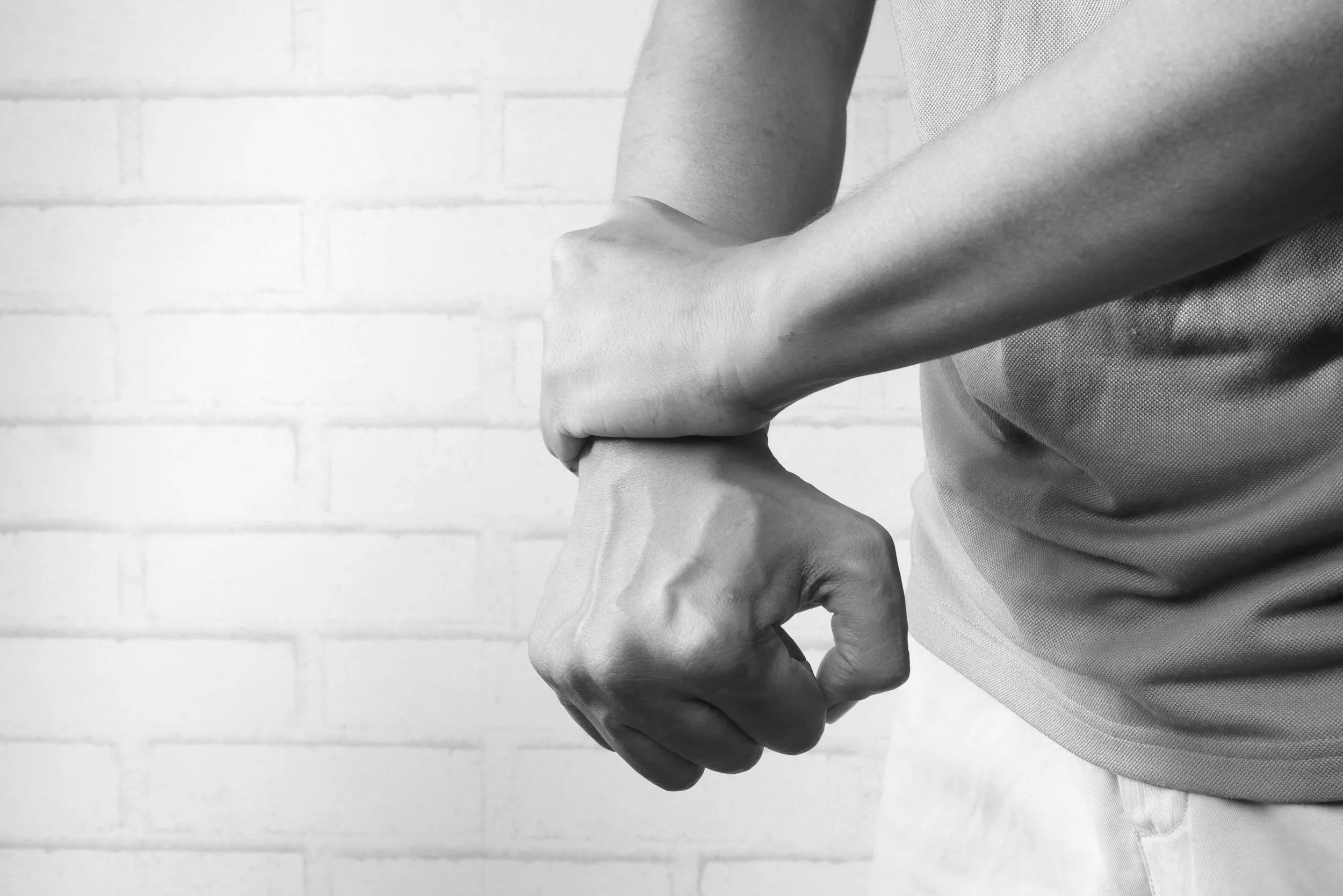 A person wearing a textured shirt shaking hands with another person against a white brick wall background.