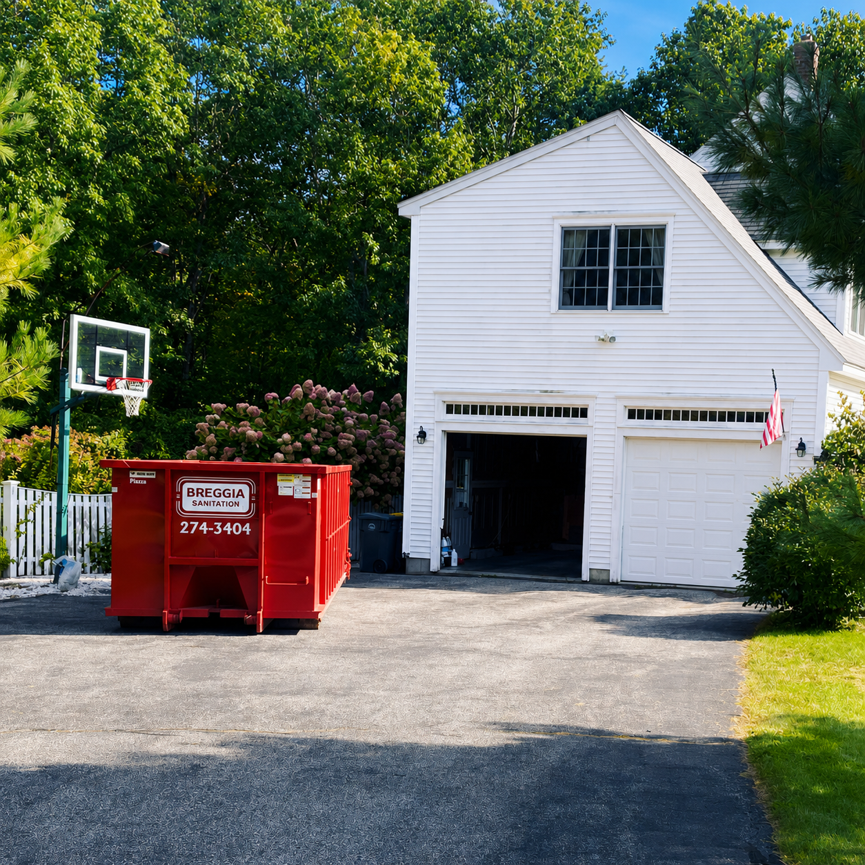 Dumpster in a driveway at a residential white garage with a basketball hoop
